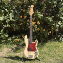 Bílá elektrická basová kytara s červeným pickguardem a javorovým hmatníkem. Na hlavě nástroje je viditelné logo Fender. Kytara stojí na černém stojan…