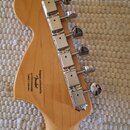 Zadní strana hlavy kytary z přírodního dřeva s chromovanými ladicími kolíky. Na dřevě je černý nápis: Designed and Rocked by Fender s číslem s.n. US1…