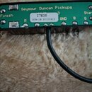 Detail zelené tiskované spojnice s nápisem Seymour Duncan Pickups. Na bílém štítku je uvedeno I7K38 a SCR-1N 20100412. Na desce jsou dále viditelné o…