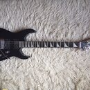 Černá elektrická kytara s šiputým tělem a hrotovou hlavou. Na hlavě je bílý nápis Jackson. Nástroj má dva humbuckery, tremolo most a trojúhelníkové h…