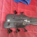 Černá hlava basové kytary s čtyřmi ladicími kolíky. Na povrchu je bílé logo ve tvaru písmene „W“ a nápis „Thump Bass“. Povrch vykazuje drobné oděrky…