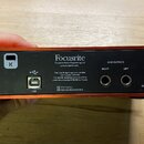 Zadní strana červeného audio rozhraní značky Focusrite. Je zde USB port, dva výstupy s nápisy LINE OUTPUTS RIGHT a LEFT a štítek s texty Focusrite, F…