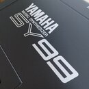 Detailní záběr na černý povrch hudebního nástroje. Je zde vidět bílý nápis YAMAHA, pod kterým je menším písmem uvedeno MUSIC SYNTHESIZER a velký mode…