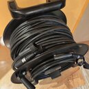 Černý kabel namotaný na plastovém navíjači s rukojetí. Na kabelu je viditelný konektor XLR a plastová svorka pro upevnění. Povrch navíjače vykazuje m…