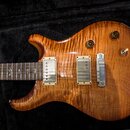 Elektrická kytara s tělem z plamenového javoru v medové barvě. Nástroj má dva humbuckery s krémovými rámečky, jeden bílý přepínač a dva černé oválné…