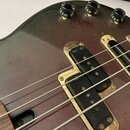 Detail korpusu basové kytary v tmavě hnědé barvě s viditnou strukturou dřeva. Nástroj má dva černé snímače a zlaté kovové části, které vykazují známk…