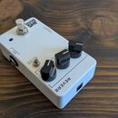 Bílý kytarový efekt s nápisem REVERB a logem JHS SERIES. Na horní straně jsou tři černé otočné knoflíky, jeden přepínací spínač s nápisem DELAY a sto…