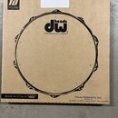 Kartonová krabice s černým potiskem stylizovaného bubnového obruče. Uprostřed je logo „dw heads“ a pod ním nápis „THE DRUMMER'S CHOICE®“. V levém hor…