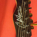Fotografie zachycuje hlavu černé elektrické kytary. Na povrchu je bílý nápis v podobě podpisu a vedle něj svisle text „CHRISTIAN GUITARS“. Nástroj má…