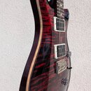 Elektrická kytara s červeně pruhovaným dřevěným povrchem a krémovým lemováním. Nástroj má dva humbuckery s bílými rámečky a chromovaný most s nápisem…