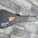 Černý tvrdý kufýr na hudební nástroj s texturovaným povrchem. V dolní levé části je bílý nápis „Gibson USA“. Uprostřed je nalepená oranžová nálepka s…