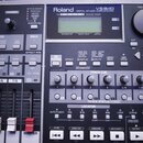 Šedý digitální záznamový studiový mixážní pult s nápisem Roland DIGITAL STUDIO WORKSTATION VS-840. Zařízení obsahuje LCD displej, několik posuvníků,…