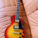 Elektrická kytara s trupem v červeno-žlutém sunburst provedení a viditnou strukturou dřeva. Na hlavě hmatníku je nápis Epiphone. Nástroj má dva humbu…