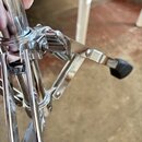 Detailní pohled na chromovaný kovový mechanismus stojanu s nožním pedálem. Pedál má na konci černou gumovou nebo plastovou nástavbu. Povrch chromu vy…