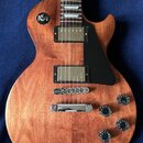Elektrická kytara s hnědým dřevěným povrchem a černým plechtrátem. Nástroj má dva humbuckery s kovovými kryty, čtyři černé otočné knoflíky a přepínač…