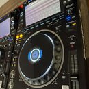 Černý digitální DJ player s displejem a velkým ovládacím jog-kolem. Na přístroji jsou viditelné nápisy Pioneer DJ a MULTI PLAYER CDJ-3000. Povrch je…