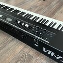 Černý digitální klavír s bílými a černými klávesami. Na levé straně je bílé logo Roland a vpravo nápis VR-730. Ovládací panel obsahuje displej, někol…