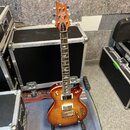 Elektrická kytara s trupem v žlutě-oranžovém sunburst provedení a hnědým hmatníkem. Na hlavě je bílý nápis "Schecter". Hmatník obsahuje bílé vložky v…