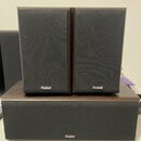 Tři reproduktory značky Magnat s černými textilními kryty a tmavým dřevěným povrchem. Dva menší stolní reproduktory stojí vedle sebe nad jedním širší…
