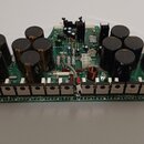 Fotografie zobrazuje zelenou základní desku s elektronickými komponenty. Na desce jsou rozmístěny velké černé válcové kondenzátory, množství rezistor…