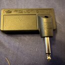 Černý plastový adaptér s kovovým jack konektorem. Na horní straně je text: MODEL: AMPLUS MADE IN JAPAN BATTERY: AAA SIZE (LR03, LR04, R10) 1.5V x 2 P…