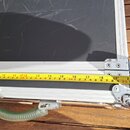 Detailní pohled na spodní část černého transportního kufru s hliníkovým profilem a kovovým povesem. Přes spodní hranu je přiloženo žluté krejslové me…