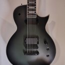 Kytara s matně černým povrchem těla a hnedým hmatníkem s bílými vložkami. Nástroj má dva humbuckery, přičemž na spodním je viditelné logo EMG. Na těl…