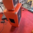 Kytarový kombozesilovač složený z hlavy a kabinetu v oranžovém potahu. Na předním panelu hlavy je viditelné logo Orange. Povrch nástroje vykazuje běž…