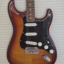 Elektrická kytara s trupem v červenohnědém sunburst provedení a černým pickguardem. Nástroj má tři bílé snímače typu single-coil, chromovaný kobylník…