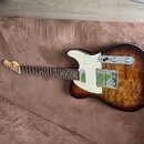Elektrická kytara s prohnutým korpusem v tmavě hnědém sunburst provedení s viditnou strukturou dřeva. Nástroj má bílý pickguard, dva snímače a stříbr…