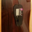 Černý digitální ladič značky Ashlan s nápisem AUTOMATIC CHROMATIC TUNER a POWER, který je namontován na hnědém dřevěném povrchu nástroje. Displej je…