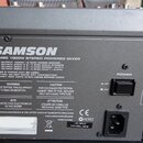 Zadní strana šedého mixážního pultu s nápisem SAMSON a označením TXM20 1000W STEREO POWERED MIXER. Na zařízení jsou vidět několik varovných štítků v…