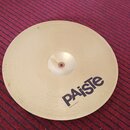 Kruhový mosazný činel s viditelným rýhováním povrchu. Na spodní části je tmavě modrý nápis PAiSte a pod ním menší text MADE IN GERMANY. Povrch je v d…