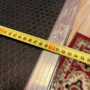 Černý přepravní kufr s povrchem ve tvaru včelího plástre. Má hliníkové hrany a rohové prvky. Přes kufr je položen žlutý metr, který ukazuje rozměr v…