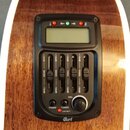 Detail na elektroniku akustické kytary s hnědým dřevěným povrchem. Černý ovládací panel obsahuje displej, pět posuvníků s nápisy +12dB a -12dB u každ…
