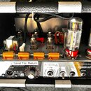 Fotografie zachycuje vnitřek kytarového zesilovače s viditelnými elektronickými komponenty. V horní části jsou umístěny čtyři malé a dvě velké elektr…