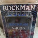 Fotografie zachycuje černý kompaktní efekt nebo zesilovač v originálním plastovém obalu. Na zařízení je nápis ROCKMAN GUITAR ACE by Tom Scholz. V poz…