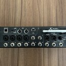 Černý digitální mixér s nápisy XAIR a XR12. Na pravé straně je bílé logo behringer v trojúhelníku. Zařízení obsahuje řadu vstupních konektorů, USB po…