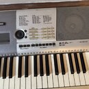 Stříbrný digitální klavír s černými a bílými klávesami. Na levé straně je logo YAMAHA a vpravo nápis PSR-E403. Horní panel obsahuje ovládací tlačítka…