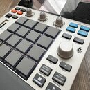Bílo-černý sampler s šedými pady a ovládacími prvky. Na horní části je červené logo AKAI Professional a nápis MPC SAMPLER. Zařízení obsahuje několik…