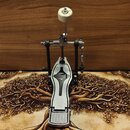 Krytý kovový pedál s černým plastovým prvkem uprostřed a stříbrným povrchem. Horní část mechanismu obsahuje bílý vlněný beater. Na zařízení nejsou vi…