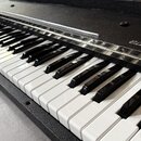Klávesnice elektronického nástroje s černým, texturovaným povrchem šasi. Na pravé straně nad klávesami je bílý nápis „Planet T“. Klávesnice má standa…