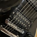 Detail černé elektrické kytary s dvěma humbuckery. Nástroj má chromovaný kobylník a jeden viditelný černý ovládací knoflík. Na lakovaném povrchu těla…