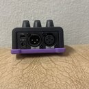 Zadní strana šedého elektronického zařízení s fialovým spodním okrajem. Jsou zde vidět tři ovládací knoflíky a konektory: USB, vstup pro napájení, vý…