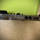 Stříbrný rackový efektový procesor s řadou konektorů na předním panelu. V levém horním rohu je částečně viditelné logo TOUSER. Panel obsahuje vstupy…