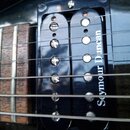 Detailní záběr na hриф kytary s dřevěným hmatníkem a dva černé humbuckery. Na pravém snímači je bílý nápis Seymour Duncan. Povrch nástroje je černý a…