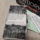 Fotka zachicuje zadní stranu kytarového efektu v šedém, texturovaném provedení. Na zadní straně je bílá nálepka s anglickým textem: „This device comp…