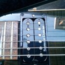 Detailní záběr na hриф kytary s černým snímačem typu humbucker. Na snímači je bílý nápis Seymour Duncan. Hриф má dřevěný povrch a viditelné pražce, n…