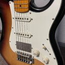 Elektrická kytara s trupem v barevnosti sunburst a bílým pickguardem. Nástroj má tři snímače, přičemž dva horní jsou jednoduché a spodní je humbucker…