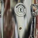 Detailzáběr na kovový korpus marcharového bubnu v chromovaném povrchu. Na korpusu je圆形 kovový štítek s nápisy MARCHING, Performer Line a logem t v kr…